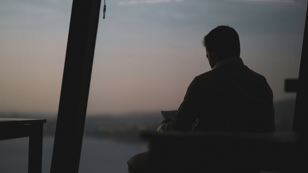Silhouette of man in office looking out window at sunrise city skyline, representing ambition, reflection, and modern professional lifestyle