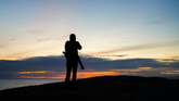 Man silhouetted with backpack standing at coastal cliffside at sunset — NO&YO You Don't Need a Reason to Go