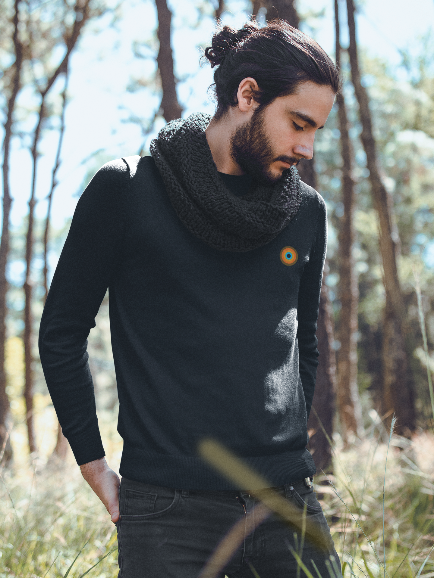 Man wearing NO&YO Heather Black crewneck sweatshirt with scarf, leaning against tree in forest, luxury outdoor apparel style.