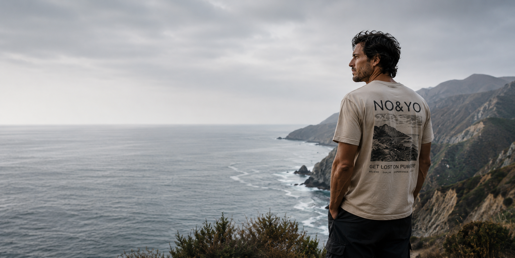 Man wearing NO&YO adventure apparel overlooking a rugged coastline.